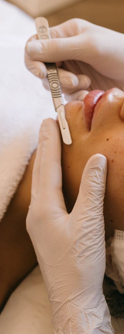A dermaplaning treatment in progress at Enhance-Her, a sterile blade held flush to the skin.